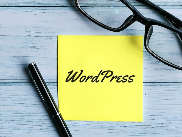 Gelber Notizzettel mit dem Wort „WordPress“, daneben ein Stift und eine Brille – Symbolbild für professionelle WordPress Website von Webella Design Schweiz.